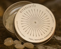 Open Ritualistic tin with mastic tears on warm stone.