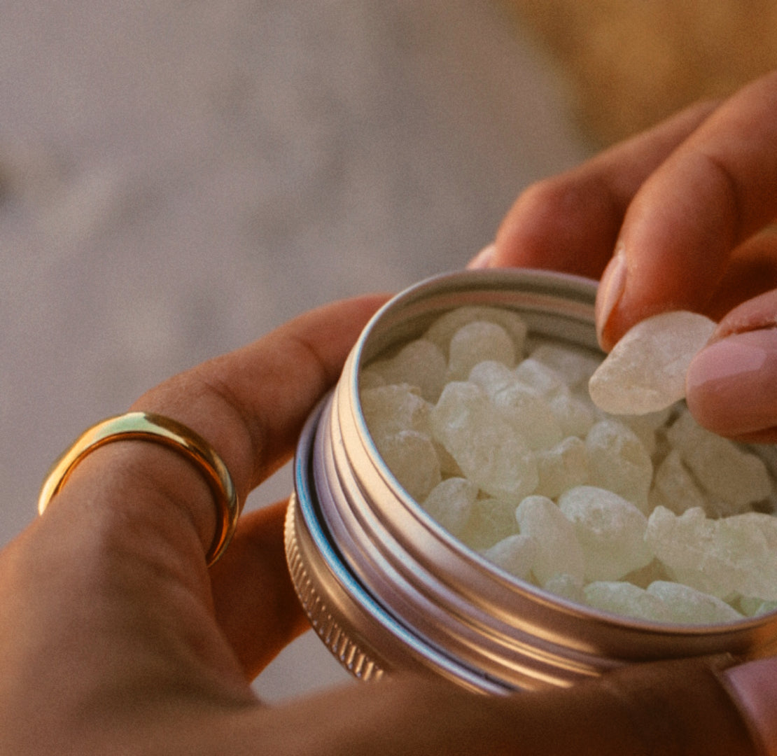 Hands lifting a tear of mastic resin from an open tin.